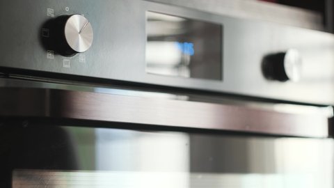 Close-up of woman turning oven handle. Concept. Woman switches modes on oven panel for baking. Woman sets up oven for cooking. Kitchen equipment