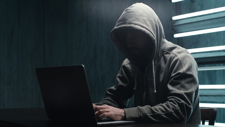 Unrecognizable man hacker wearing sweatshirt with hood typing on laptop computer keyboard and breaking password. Side view of dangerous hooded computer hacker infecting system with cyber virus. | Shutterstock HD Video #1064121997