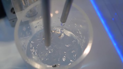 Super slow motion: droplets falling from tube - compact liquid dosing system: close up. Automated technology, measuring, pharmaceutical, healthcare, laboratory equipment concept