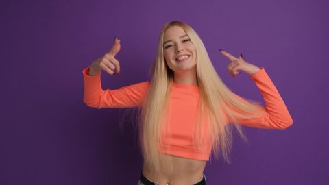 Positive blonde happy dancing and having fun in the studio on a purple background.