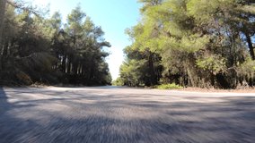 Fast tracking POV video from asphalt road perspective through a winding forest road with with clear blue skies