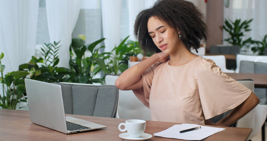 Curly-haired african american woman freelancer sitting in cafe restaurant working remotely from public place feels pain suffers from injury in back arthritis holding on to spine, disease problems Royalty-Free Stock Footage #1064126890
