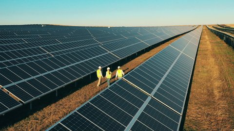Aerial shot of three solar energy engineers on a large solar farm