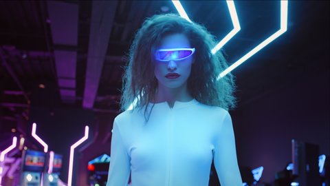 Fashion young woman in futuristic glasses and white suit walk in night club in city. Blue and violet neon lights. AR hybrid reality, future technology, augmented reality, entertainment, sci-fi concept