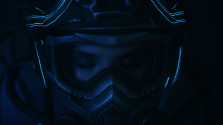 Portrait female soldier of future in fiction helmet open her eyes looking into camera standing on black background at night. Woman in futuristic combat costume. Cyberpunk style warrior Royalty-Free Stock Footage #1064129500