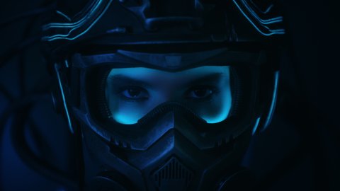 Portrait female soldier of future in fiction helmet open her eyes looking into camera standing on black background at night. Woman in futuristic combat costume. Cyberpunk style warrior