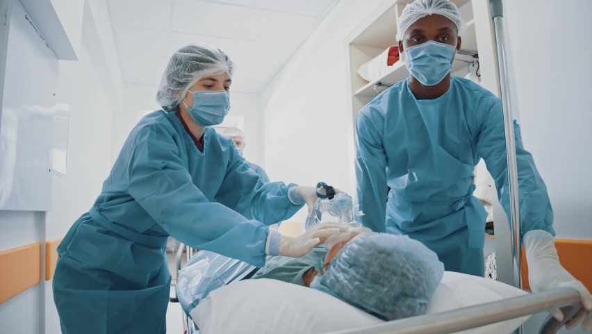 Mixed race paramedics walking in hospital hallway taking injured consciousless patient to the operation room. Surgery concept. Emergency department. Royalty-Free Stock Footage #1064129995
