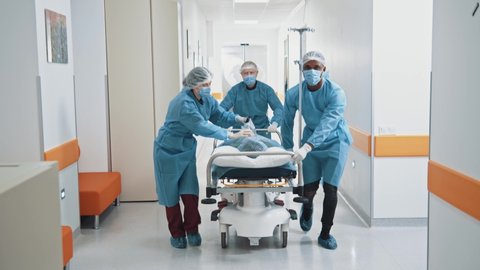 Emergency department: doctors, nurses and surgeons moving seriously injured patient lying on a stretcher through hospital corridors. Medical staff in hurry move patient into operating theater concept