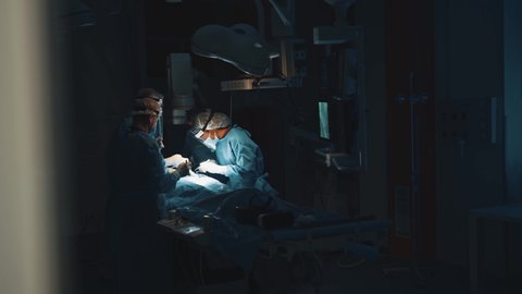 In dark hospital room multi-ethnic surgeons working on open chest surgical operation. Healthcare. Cooperation. Emergency department. Medical concept.