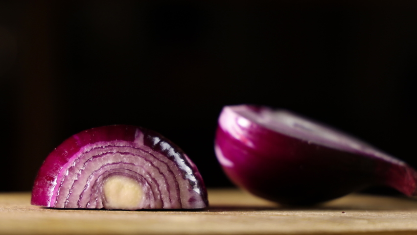 Female hands cut onions in the kitchen. Macro shooting of red onions. The woman cuts onions on a wooden board.