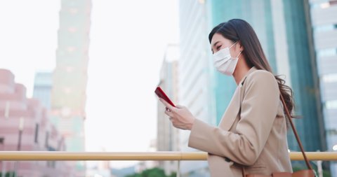 asian woman use smartphone outdoor with face mask while commuting