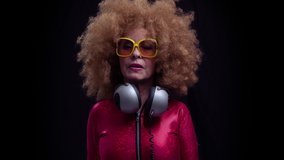 Funky grandmother with afro hairstyle and headphones around neck dancing in nightclub