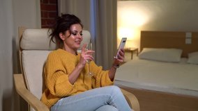 cheerful lady is drinking champagne alone at home and chatting online by smartphone with friends