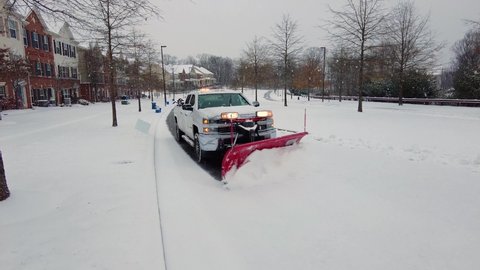 Clarksburg, Maryland, USA 12-16-2020: A Chevy Silverado pickup truck equipped with snow plow attachment is removing accumulation in roads at frozen residential suburban neighborhood under heavy snow.