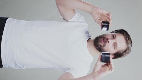 Vertical video of happy bearded attractive funny man juggling jars pf moisturizing cream showing and advertising on studio background. Concept for cosmetics.