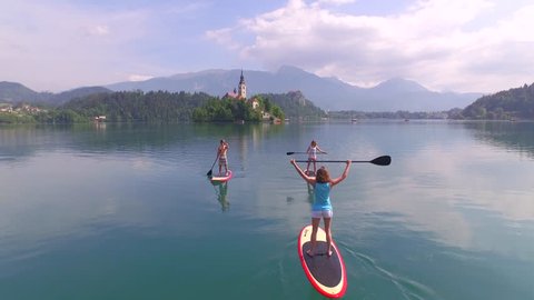 AERIAL: Cheerful young couple and a friend meeting while paddling on SUP boards on the bled lake स्टॉक व्हिडिओ