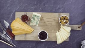 Time lapse. Flat lay. Arranging gourmet cheese, crakers, and fruits on a board for a large cheese board.
