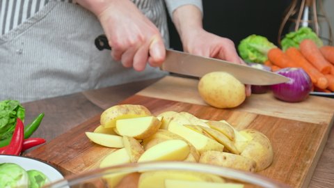 A close-up look of slicing fresh potatoes on a wooden cutting board in 4k. Concept of chopping fresh potatoes as a vegetable for roast chicken along with other vegetables on the table.