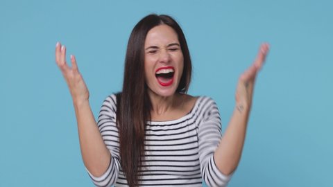 Angry irritated brunette young woman 20s years old wearing basic casual striped shirt posing isolated on blue color background in studio. People lifestyle concept. Spreading hands screaming swearing