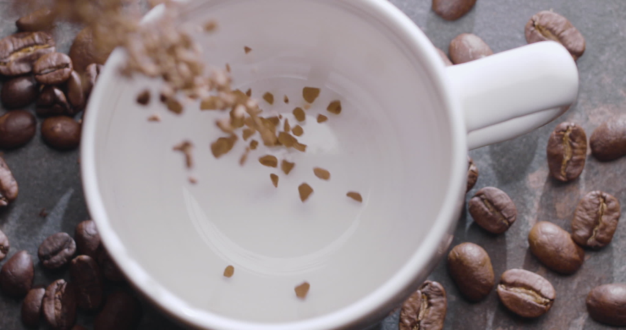Instant coffee granules are poured into a white cup, then boiling water is poured, slow motion, macro top view. 300fps, Blackmagic Ursa Pro G2.  Royalty-Free Stock Footage #1064161975