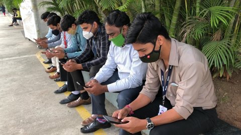 Pune, India - December 17 2020: Indian men sitting and using mobile phone outdoors at Pune India.