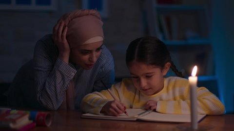 Mother and daughter in hijab doing homework using candles for illumination. Education Concept.