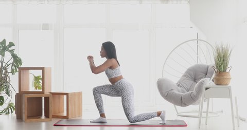 Sporty young black woman making back lunges training at home. Athletic fit girl doing fitness aerobic exercises for booty in living room. Home fitness and wellness concept.