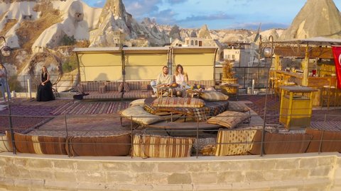 Happy couple on rooftop of an cave house enjoying brackfast and of Goreme city panorama, , Cappadocia, Turkey. Aerial view 4K.