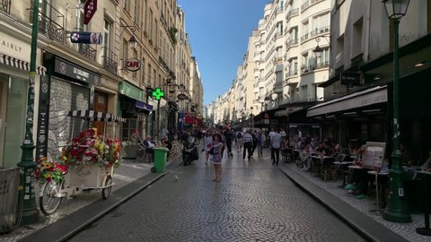 PARIS - CIRCA AUGUST, 2019: Footage of people walking and sitting at cafes on famous street called "Rue Montorgueil" in Paris. It is a sunny summer day. Camera moves forward.