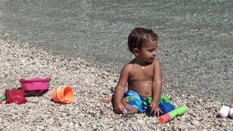 Zoom in face of toddler with beach toys on pebbles

