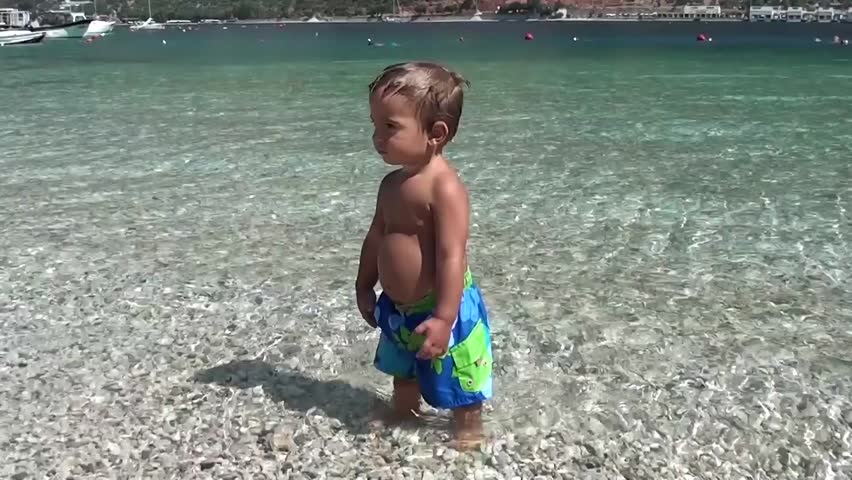 Zoom in potbelly of a child in sea water staring and walking away
