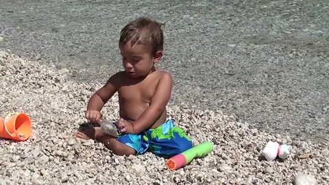 Toddler with beach toys on pebbles
