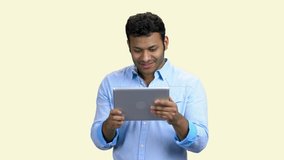 Cheerful Indian man with tablet pc on white background. Happy excited young man talking via internet using digital tablet.