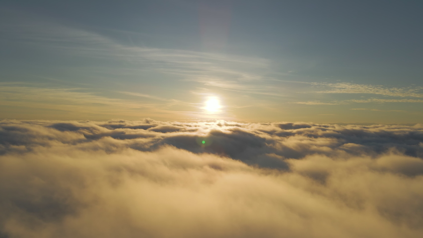 Aerial view of bright yellow sunset over white dense clouds with blue sky overhead.