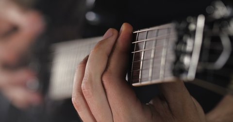 Unrecognizable rock musician in black clothes plays black electric guitar on black background isolated and smoke. Close up detail shot of hands and guitar neck, Shallow focus