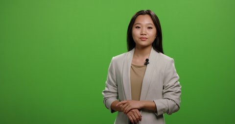 Positive asian woman looking at camera and talking during an advertisement. Female anchor during morning news report, shot on green background 4k footage