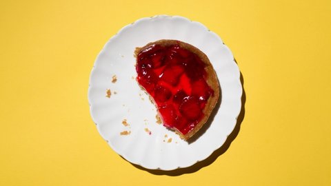 Eating strawberry cheesecake bite by bite, stop motion. Plate of cake moving in the frame. Food animation, top view, light yellow background