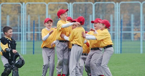 Baseball at school, a team of boys baseball players in yellow uniforms get hugs and rejoices in victory, successful game, positive emotions, 4k Slow Motion.
