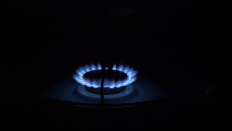 Gas burner on, glowing with blue flame, at night in the kitchen. Close-up. Gas stove on black background. A dangerous method of heating room. Natural gas is burning. 4K.