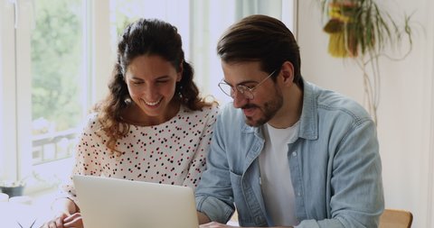 Happy millennial caucasian family couple looking at computer screen, discussing purchases in online store, choosing films for evening watching, web surfing hotels planning summer vacation together.