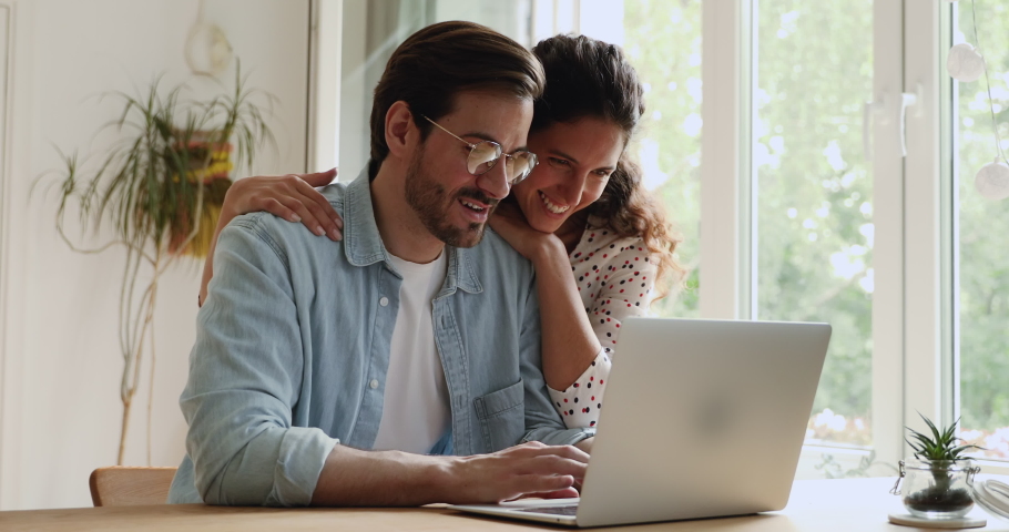 Loving millennial caucasian bonding couple using computer, planning honeymoon or summer vacation, watching family photos, web surfing information or enjoying online shopping together at home. | Shutterstock HD Video #1064201593