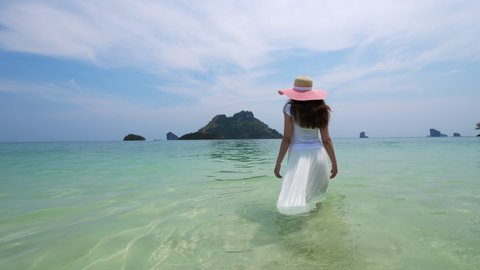 Amazing tropical sea, woman walk at sandy shelf, long skirt in water. Tourist lady slowly move deeper, touch warm water by hand. Happy vacation time at breathtaking islands of Thailand
