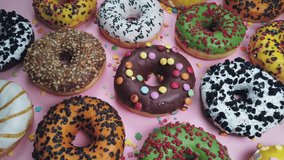 assorted donuts with icing a pink background. Background of assorted doughnuts with different flavors. The video dolly