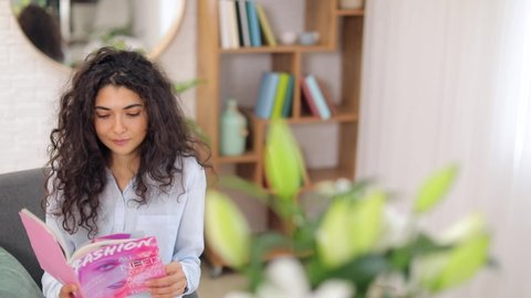 Bouquet of beautiful lilies in room of young woman reading magazine