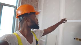 Afro renovation worker blogger filming video about apartment redecoration. African male builder in uniform having video call showing customer process of house renovation
