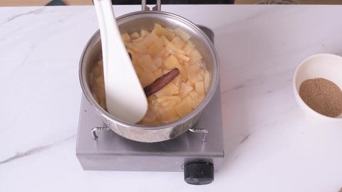 Boiling apple sauce with cinnamon branch on white marble side view