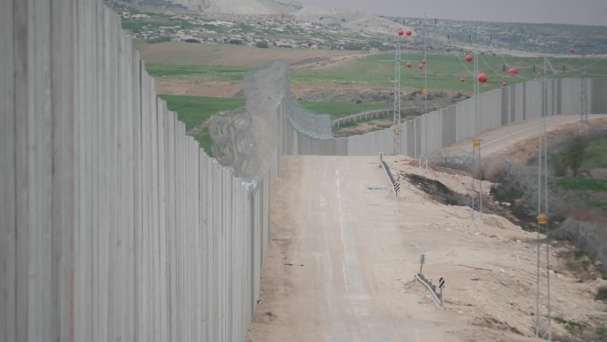 The separating wall between Israel and the Palestinian territories with a road next to it. a telephoto shot with a long perspective, showing the length and size of that land divider, Israel.