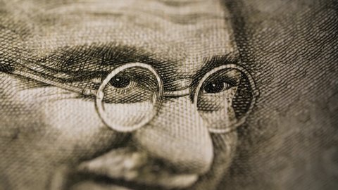 Dramatic close of eyes of Mahatma Gandhi on Rupee bill with flashing light. Extreme details of Indian currency. Angry symbol for nonviolent resistance and civil rights freedom movements. 4K.