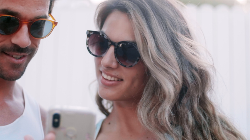 Couple looking at a smartphone outdoors in the summer, Girl taking off the sunglasses