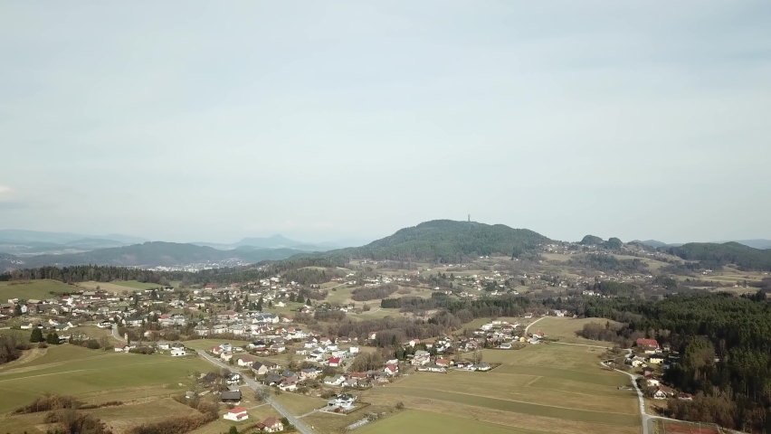 A drone capture of an Alpine ladscape in Austria. There are many small villages at the foothill of higher mountains. Lots of forest area. High mountain chains in the back. A vast lake in the back
